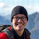 Adventurer David Chen in hiking gear, smiling in a mountainous landscape.